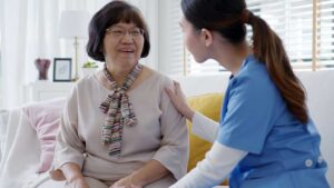 Older resident and caregiver discussing a meal plan and religious items in a bright assisted living room.